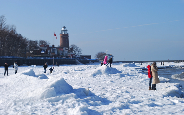 Kolobrzeg im Winter©Olga Korowacka - stock.adobe.com Leuchtturm an einer verschneiten Küste mit Menschen auf dem Eis.