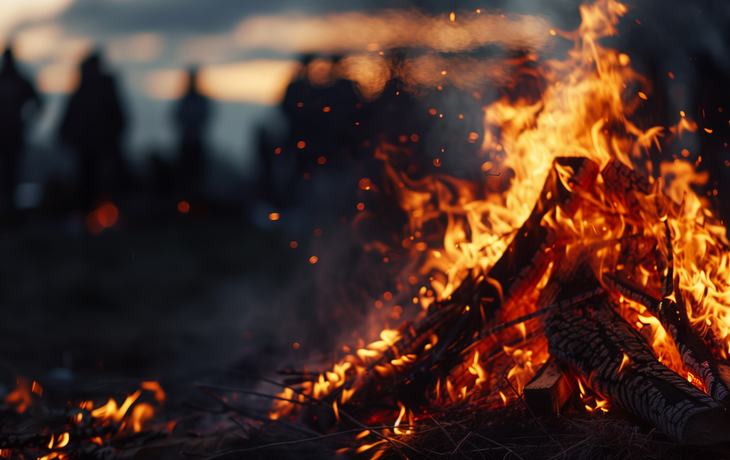 Feuer mit Menschen im Hintergrund bei Dämmerung.