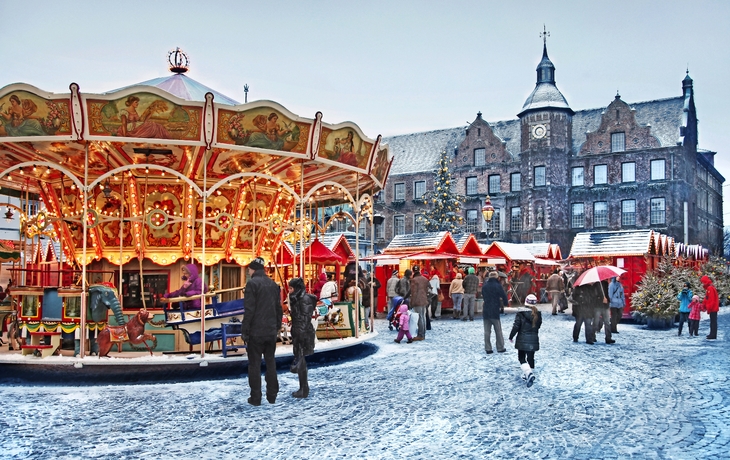 Karussell und Menschen auf winterlichem Weihnachtsmarkt vor historischem Gebäude.