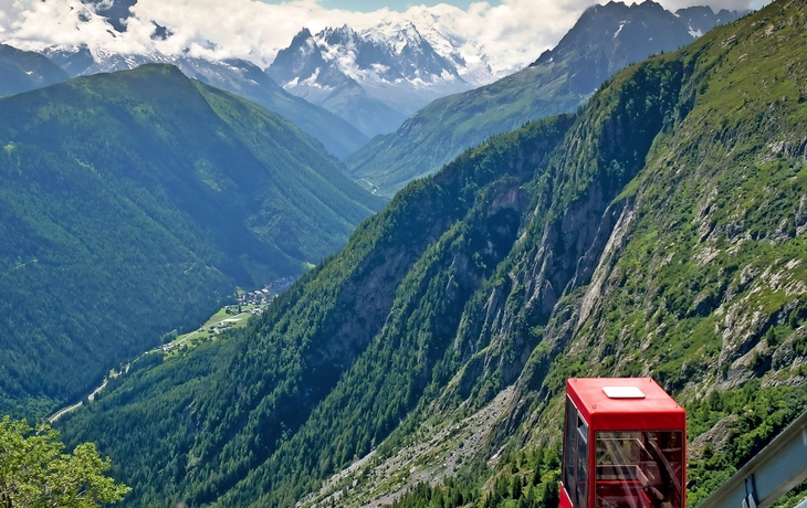 Rote Bergbahn in alpiner Landschaft mit Tal und schneebedeckten Bergen im Hintergrund.