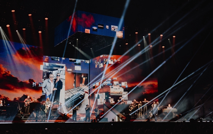 Bühnenauftritt mit Band und beeindruckender Lichtshow in einer großen Arena.