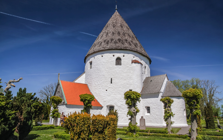 Rundkirche auf Bornholm, umgeben von grüner Landschaft und blauem Himmel.