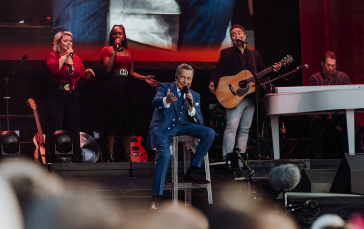 Musiker auf Bühne mit Instrumenten und Sängern im Hintergrund