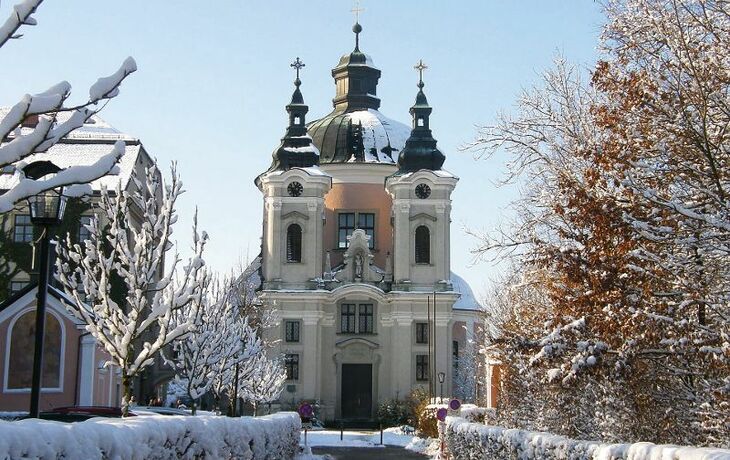 Wallfahrtskirche Christkindl im Winter mit Schnee auf Bäumen und Wegen.
