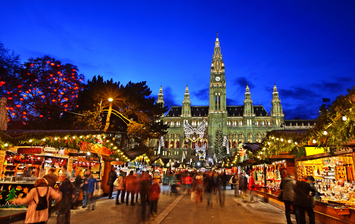 Menschen auf einem Weihnachtsmarkt vor einem beleuchteten historischen Gebäude am Abend.