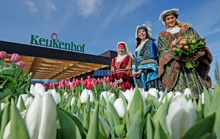 Drei Personen in traditioneller Kleidung vor dem Eingang des Keukenhofs mit Tulpen.