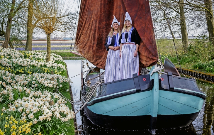 Frauen in traditioneller Kleidung auf einem Segelboot im Keukenhof, umgeben von Blumen.