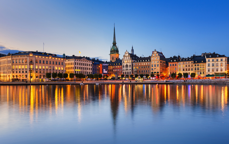 Panoramablick auf die beleuchtete Skyline von Gamla Stan in Stockholm bei Nacht, mit spiegelndem Wasser im Vordergrund.