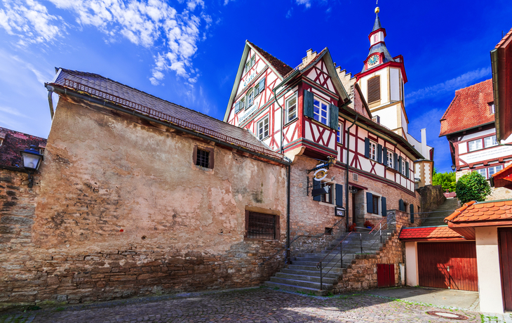 Fachwerkhaus mit Kirchturm in einer historischen Altstadt bei sonnigem Wetter.