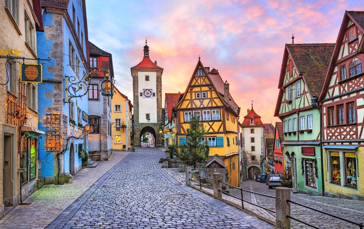 Bunte Fachwerkhäuser in einer gepflasterten Altstadtstraße bei Sonnenuntergang.
