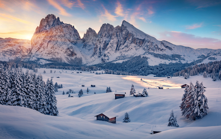 Winterliche Berglandschaft mit schneebedeckten Hütten im Sonnenuntergang.