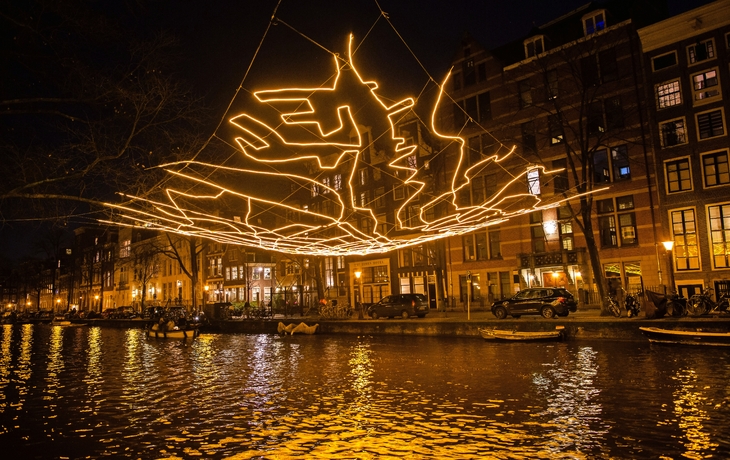 Leuchtende Stadtkarte über einem Kanal bei Nacht in Amsterdam.