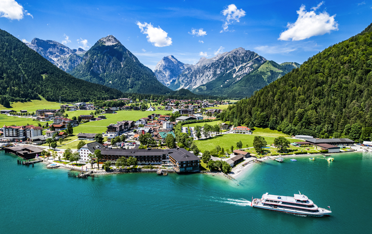 Landschaft mit Alpen, See, Dorf und Boot bei klarem Himmel.