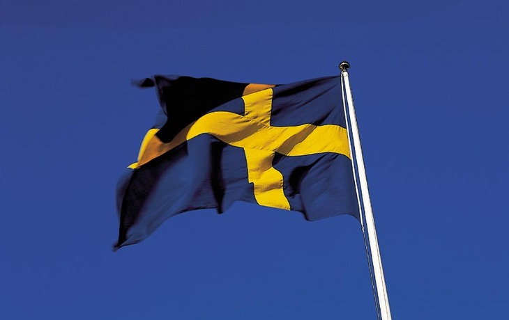 Wehende schwedische Flagge vor klarem Himmel.