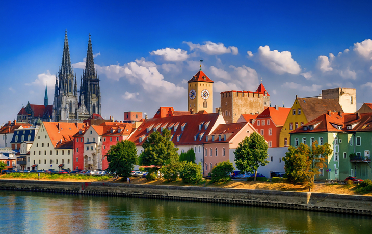 Dom St. Peter in Regensburg mit Donau im Vordergrund und historischen Gebäuden im Hintergrund.
