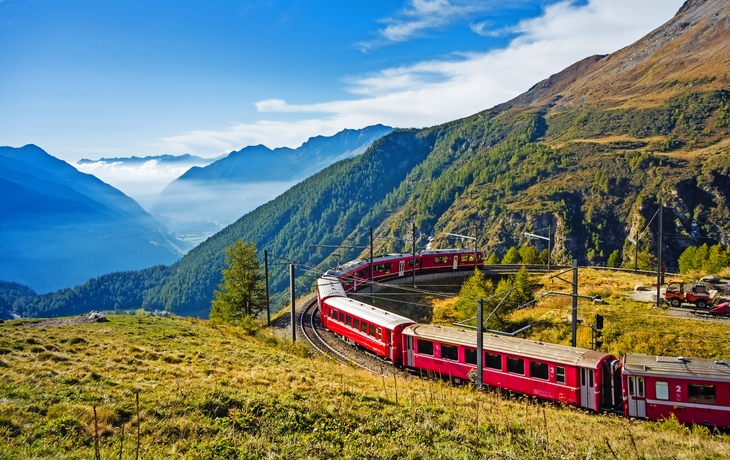 Roter Zug fährt durch malerische Berglandschaft.