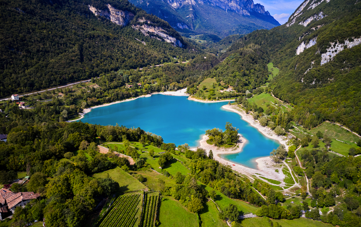 Lago di Tenno vor Alpenkulisse, umgeben von grünen Wäldern und Bergen.