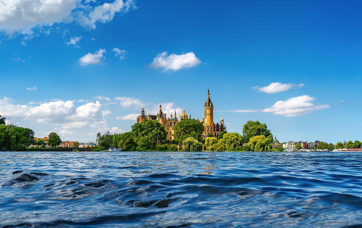 Schweriner Schloss im Sommer mit Wasser und blauem Himmel im Vordergrund.