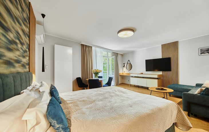 Modernes Hotelzimmer mit großem Bett, Sofa, TV und Balkonzugang.