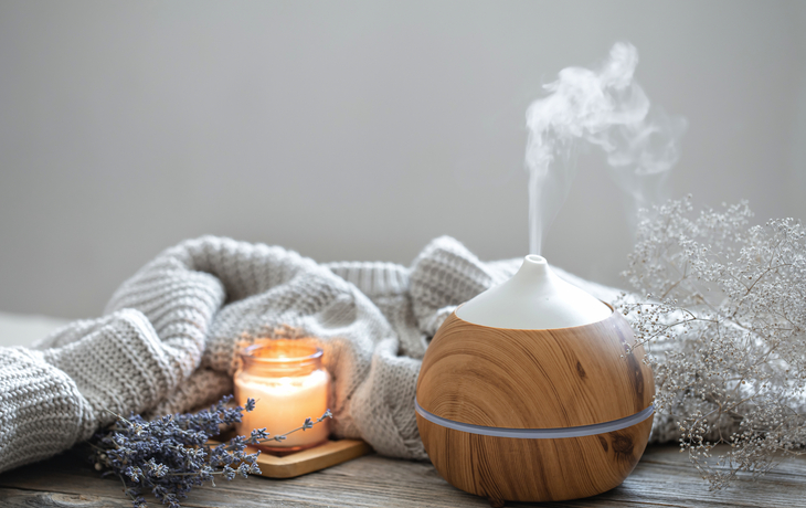 Aromadiffuser aus Holz neben brennender Kerze und Decke auf Holztisch.