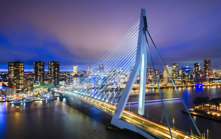 Erasmusbrücke in Rotterdam bei Nacht mit beleuchteter Skyline im Hintergrund.