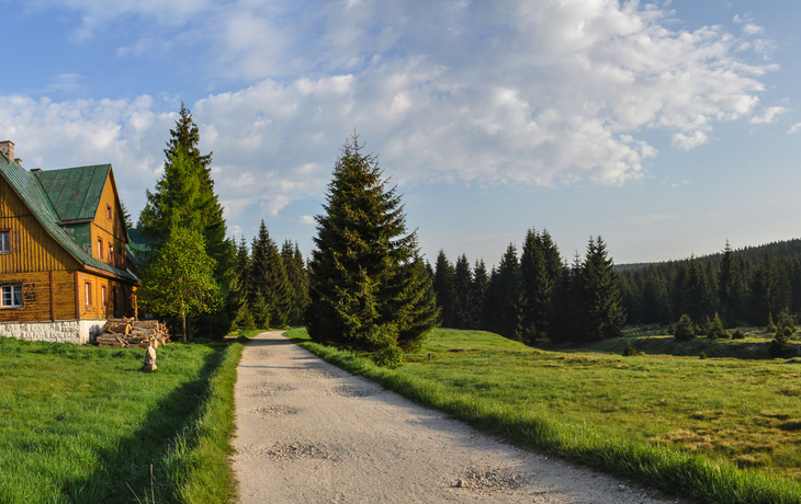 Holzhaus an einem Weg im grünen Isergebirge bei sonnigem Wetter.