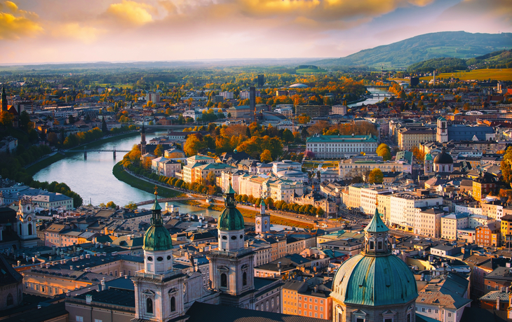 Stadtpanorama mit Fluss, historischen Gebäuden und Hügeln im Hintergrund.