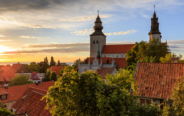 Stadtlandschaft mit Kirche und roten Dächern bei Sonnenuntergang.