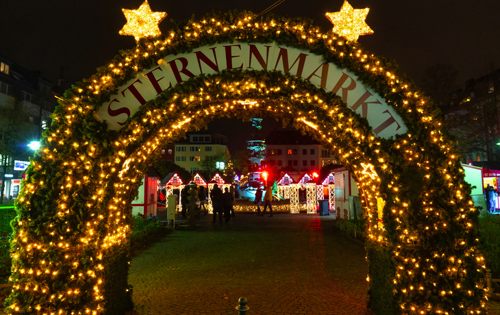 Eingang zu einem festlich beleuchteten Weihnachtsmarkt bei Nacht.