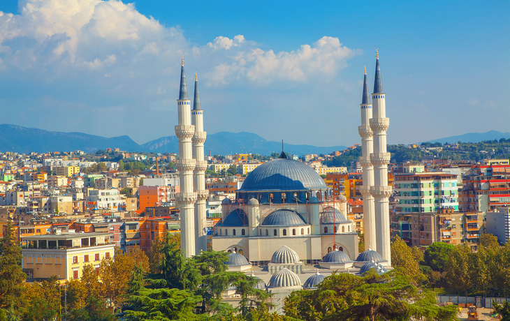 Große Moschee mit vier Minaretten vor Stadt- und Berghintergrund.