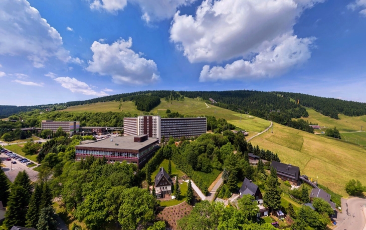 Hotelgebäude umgeben von grüner Landschaft und bewaldeten Hügeln.
