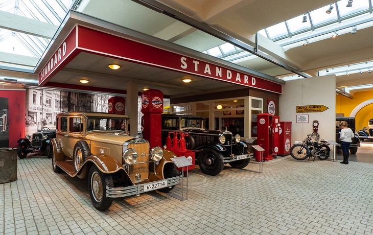 Tankstelle im Retro-Stil mit klassischen Autos und Motorrädern.