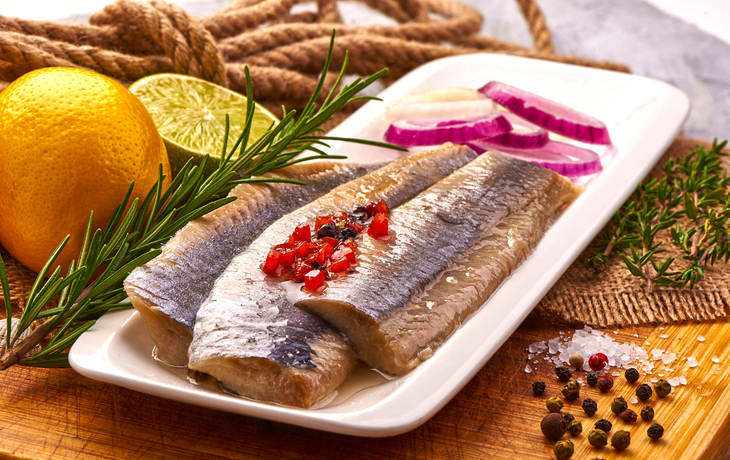 Heringsfilets mit Zwiebeln, Zitrone und Gewürzen auf einem weißen Teller.