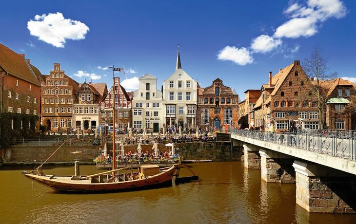 Historische Häuserfront und Boot an einem Flussufer unter blauem Himmel.