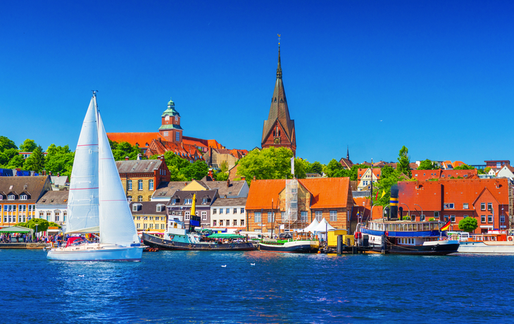 Stadtansicht von Flensburg mit Segelboot und Hafen im Vordergrund.