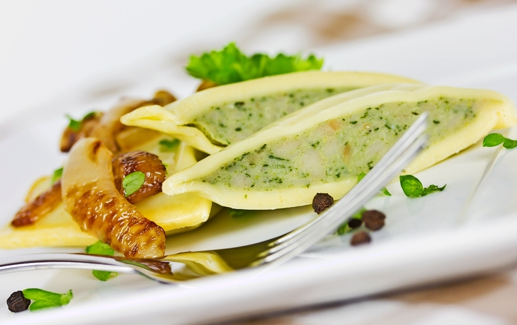 Gefüllte Teigtaschen auf einem Teller mit Pilzen und grüner Garnitur.