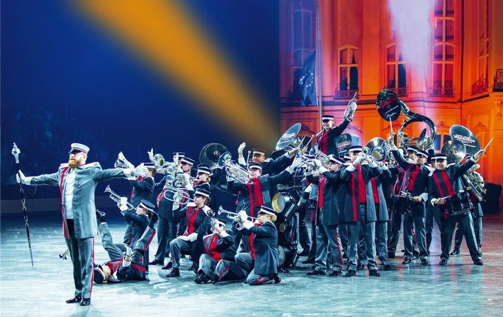 Blaskapelle in Uniformen spielt auf einer Bühne vor einem beleuchteten Hintergrund.