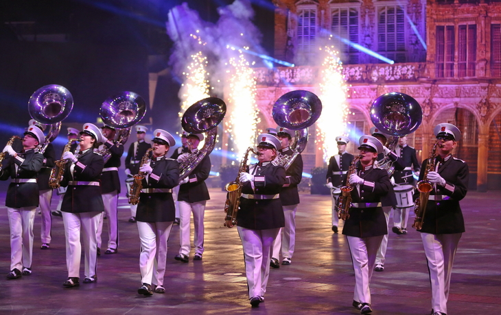 Blaskapelle in Uniformen marschiert bei einer bunten Musikparade mit Feuerwerkskulisse.