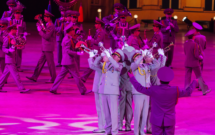 Blaskapelle in Uniform spielt Trompeten auf Bühne mit lila Beleuchtung.