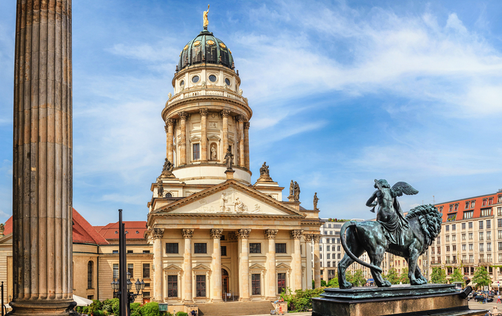 Historisches Gebäude mit Kuppel und Statue im Vordergrund bei Tageslicht.