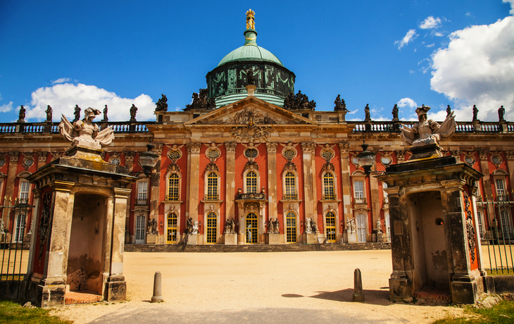 Barockes Schloss mit Kuppel, durch ein Tor gesehen, blauer Himmel im Hintergrund.