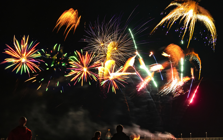 Feuerwerk am Nachthimmel mit farbenfrohen Explosionen und Menschen im Vordergrund.