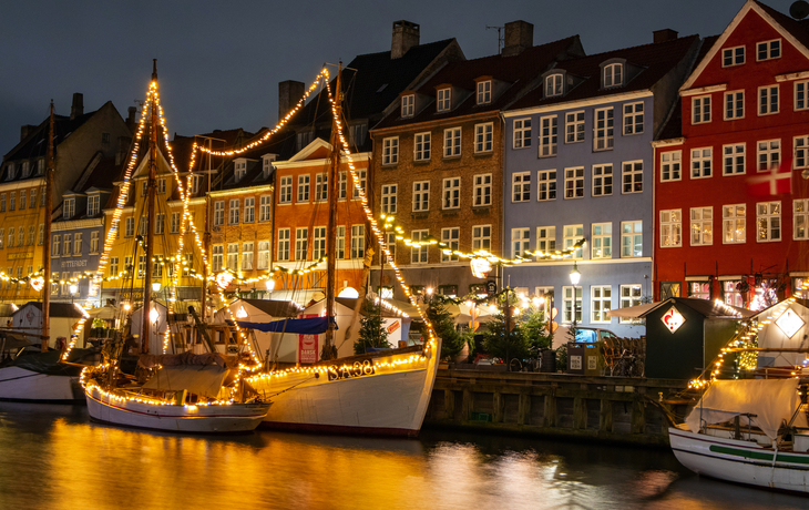 Winterlicher Nyhavn in Kopenhagen bei Nacht, beleuchtete Häuser und Boote.