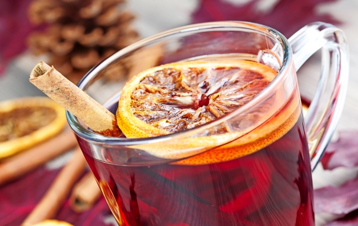 Heißer Glühwein im Glas mit Orange und Zimtstange auf Weihnachtshintergrund.