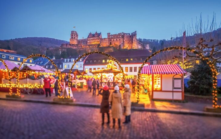 Weihnachtsmarkt mit Festbeleuchtung und Schloss im Hintergrund bei Abenddämmerung