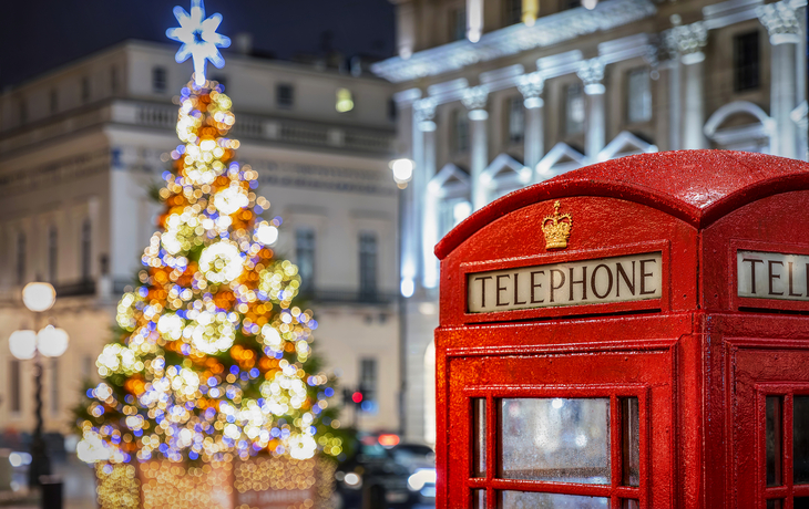Rote Telefonzelle vor einem beleuchteten Weihnachtsbaum in London während der Weihnachtszeit.