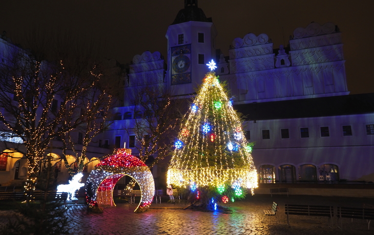 Weihnachtlich beleuchteter Platz mit beleuchtetem Baum und Tor in der Nacht.