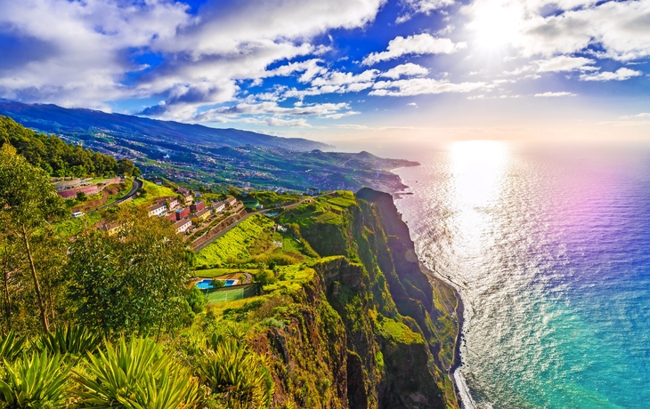 Küstenlandschaft mit steilen Klippen, grünem Vegetation und Blick auf das Meer bei Sonnenuntergang.