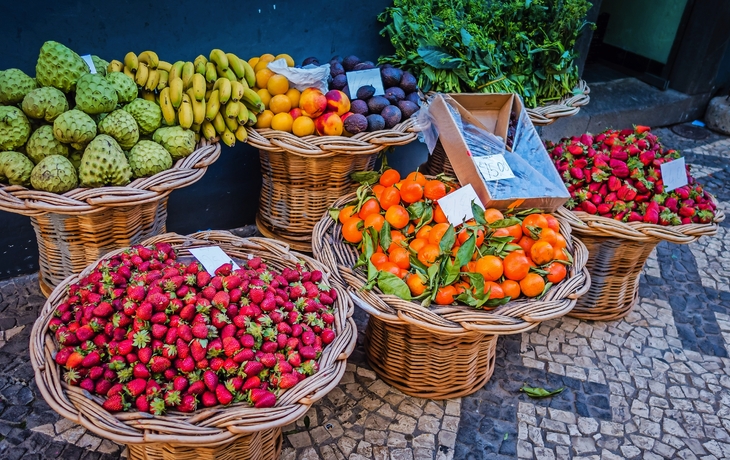 Marktstand mit Körben voller verschiedener Früchte und Gemüse.