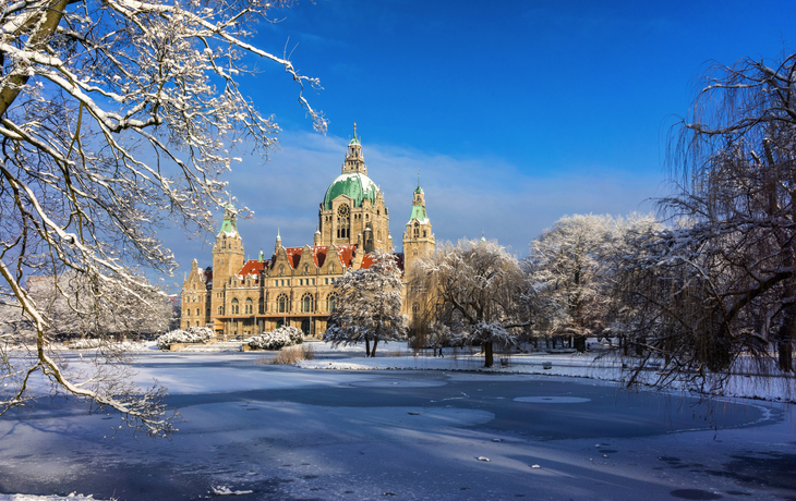 Neues Rathaus Hannover im Winter, umgeben von schneebedeckten Bäumen und zugefrorenem Teich.